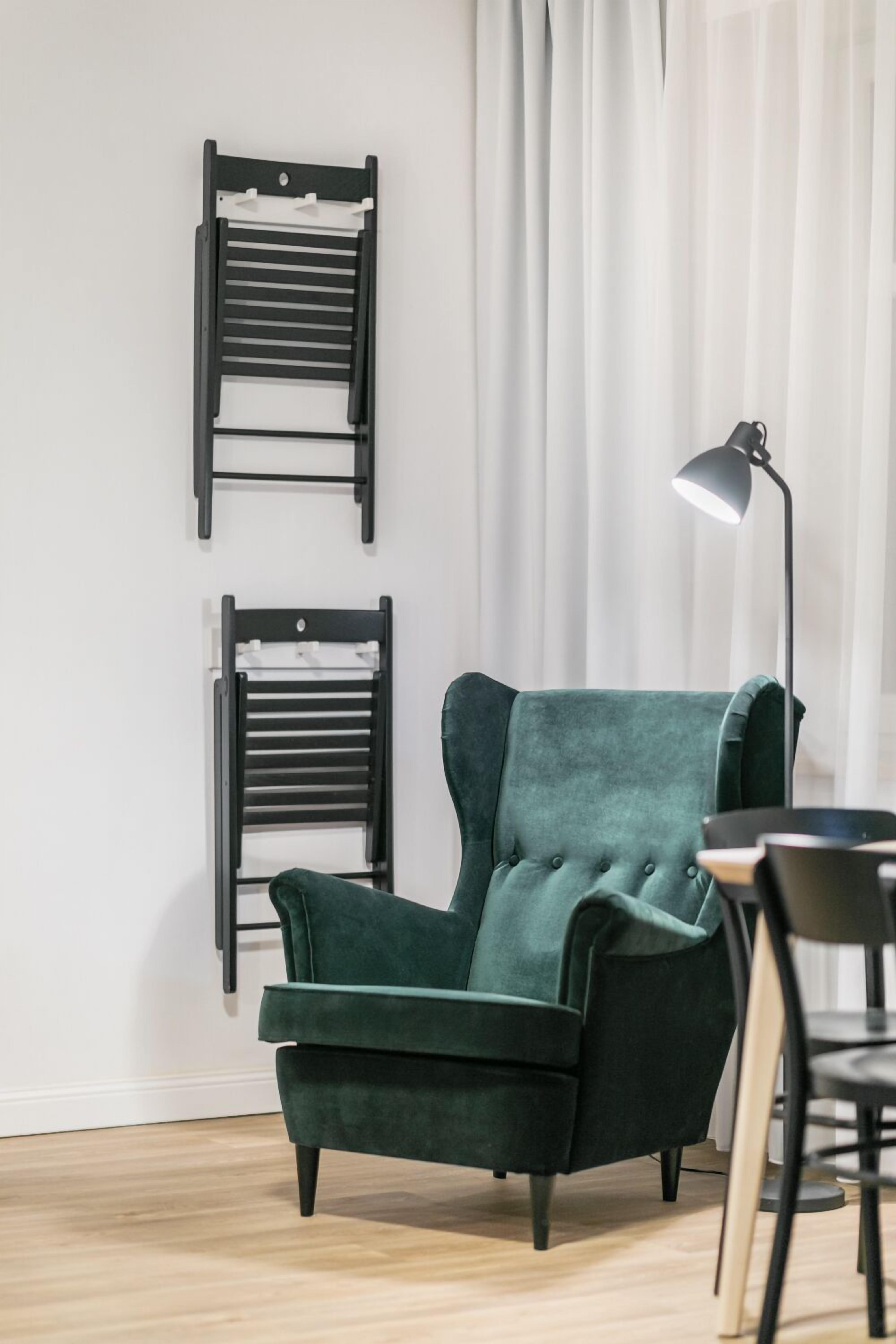 A room with a green armchair, two black chairs, a table, and a floor lamp.