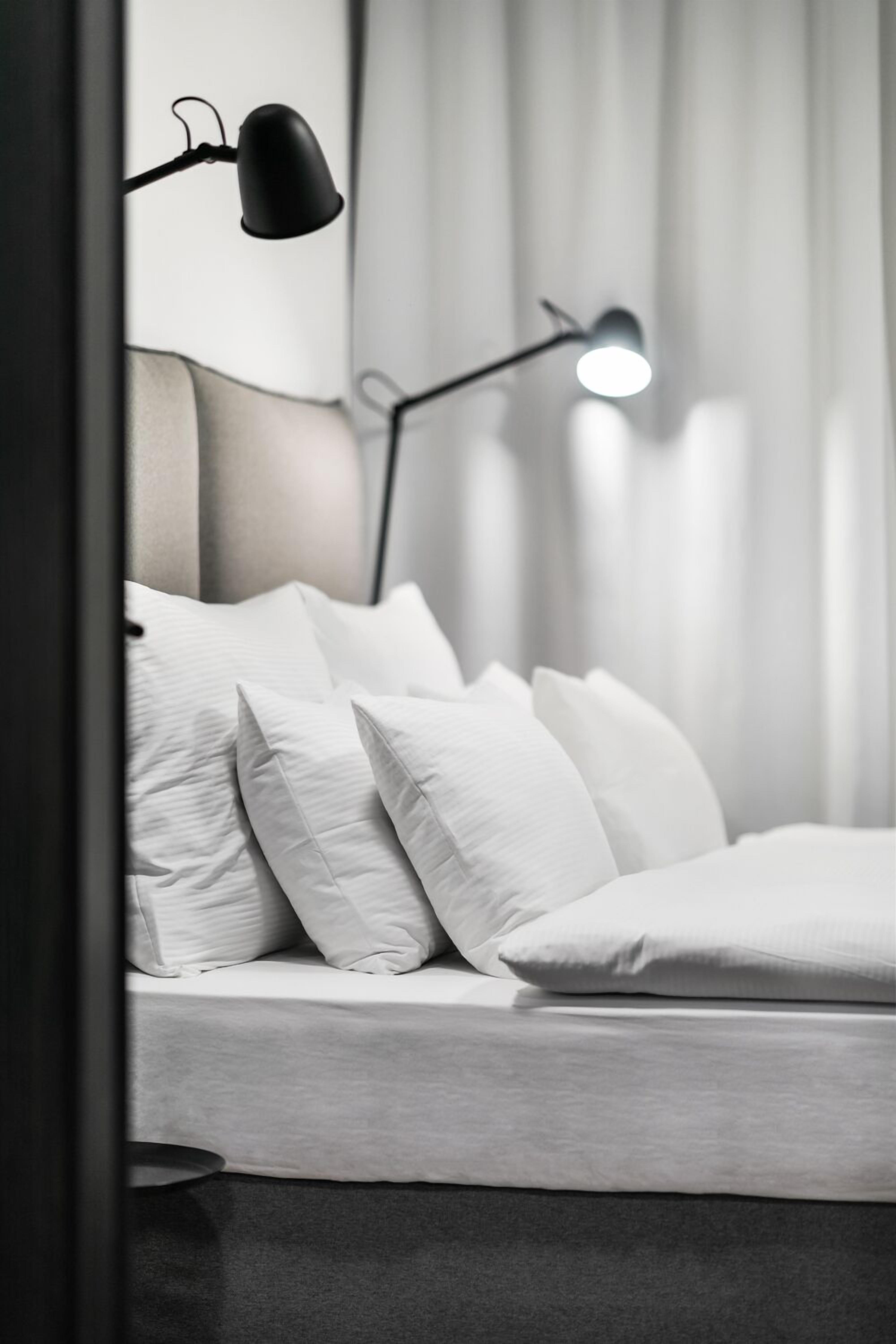 Una cama bien hecha con ropa de cama blanca y almohadas, un cabecero moderno y dos lámparas de pie negras.