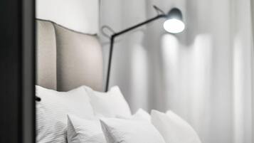 Una cama bien hecha con ropa de cama blanca y almohadas, un cabecero moderno y dos lámparas de pie negras.