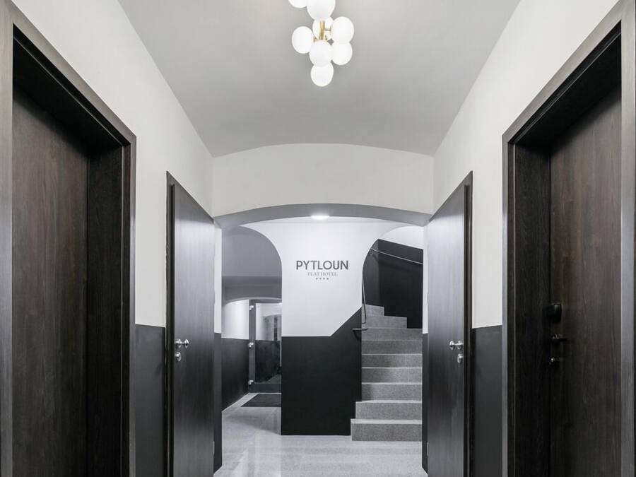 Un pasillo moderno con una escalera, puertas de madera oscura y un letrero que dice 'PYTLOUN'.
