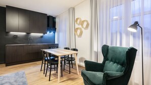 A modern kitchen with dark cabinets, a wooden dining table, and a green armchair. - Pytloun Flat Hotel (Liberec)