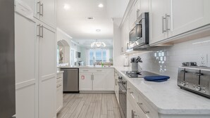 A modern kitchen with white cabinetry, stainless steel appliances, and a marble countertop. - Live in luxury in this penthouse paradise! (Fernandina Beach)
