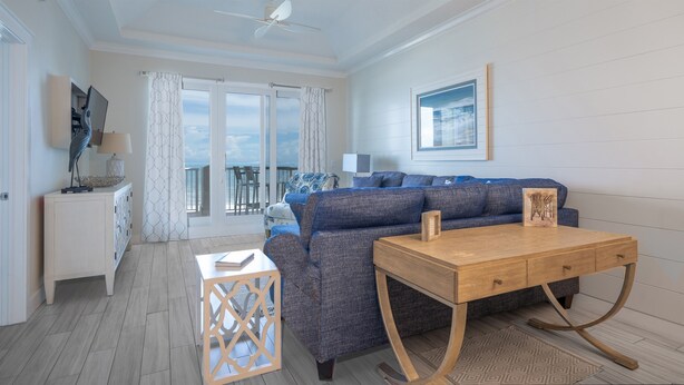 A spacious living area with a sofa, a wooden coffee table, and a view of the sea through large windows. - Live in luxury in this penthouse paradise! (Fernandina Beach)