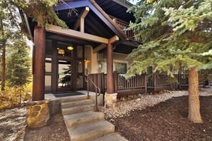 A building with a stone staircase leading to a wooden door, surrounded by trees and a gravel path.