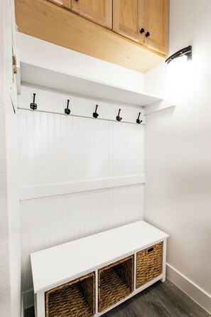A white bench with three wicker baskets underneath, a white wall with vertical paneling, and a wooden cabinet above.