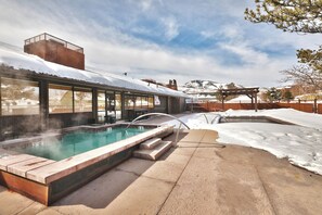 A hot tub with a wooden deck and a view of a snowy landscape.
