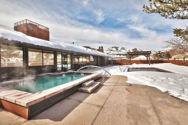 A hot tub with a wooden deck and a view of a snowy landscape.