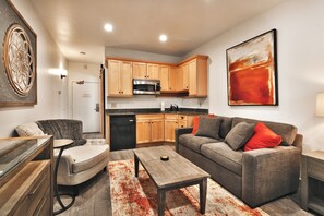 A modern living room with a grey sofa, a coffee table, and a dining area with wooden cabinets and a black refrigerator.