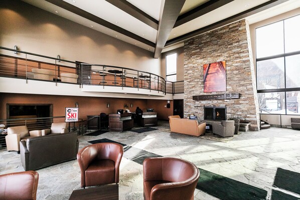 A spacious lobby with a stone fireplace, seating areas, and a ski rentals sign.