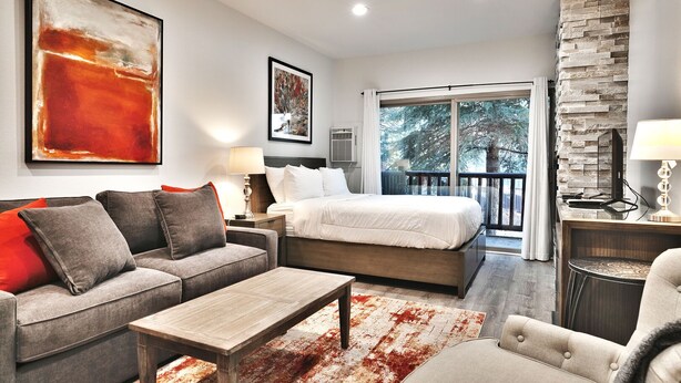 A modern hotel room with a large bed, a sofa, a coffee table, and a balcony with a stone wall. - Prospector Studio - Slps 4 (Park City)
