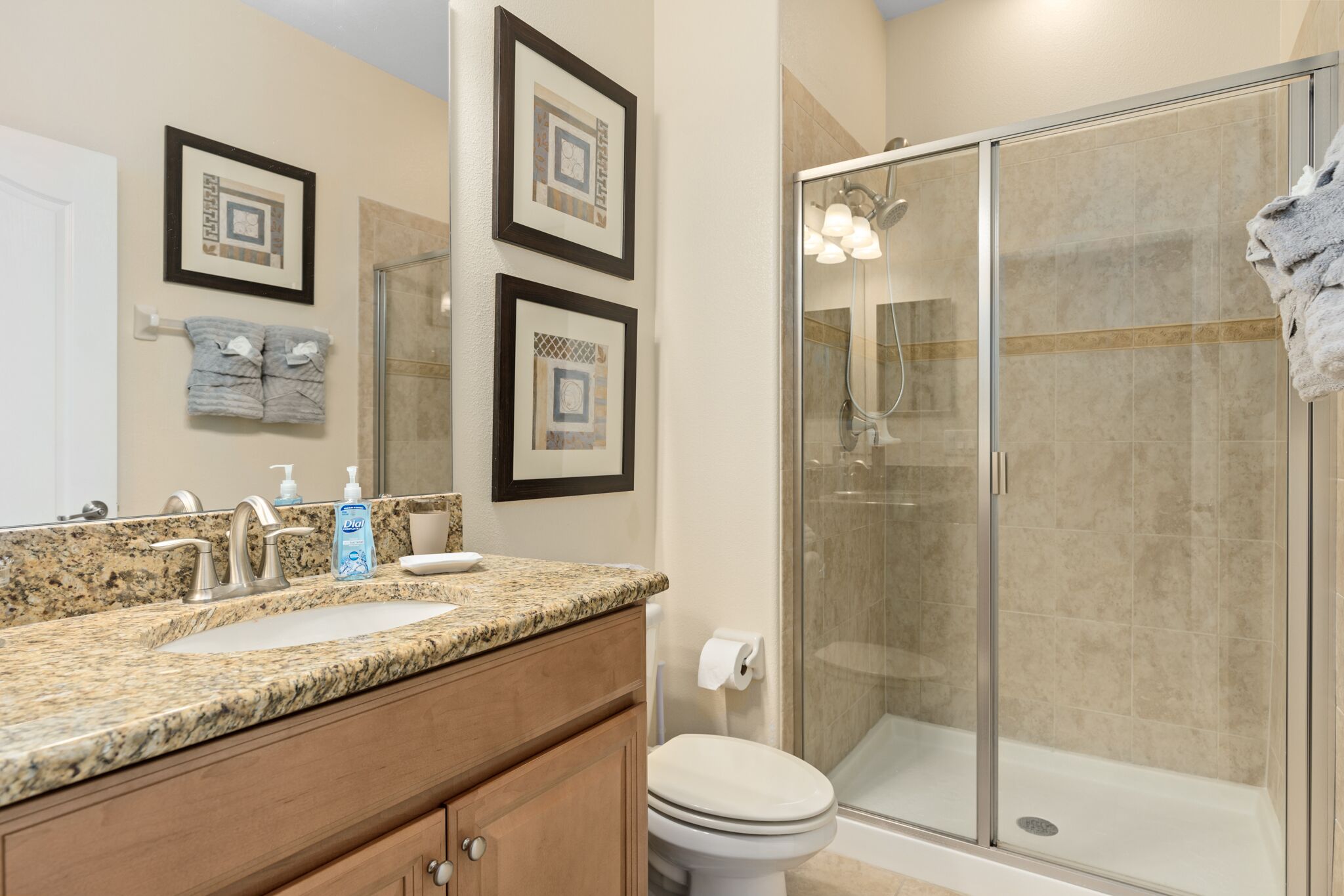 A bathroom with a granite countertop, a sink, a toilet, and a glass-enclosed shower.