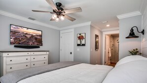 A bedroom with a bed, a ceiling fan, a TV mounted on the wall, a dresser, and a door leading to a bathroom. - The Carlton* 3 min walk to Downtown Mt. Dora!!  (Mt Dora)