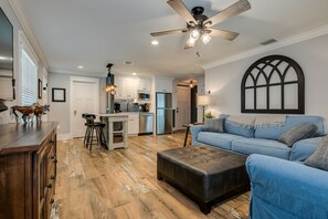 A spacious living area with a blue sofa, a wooden coffee table, and a kitchen in the background.
