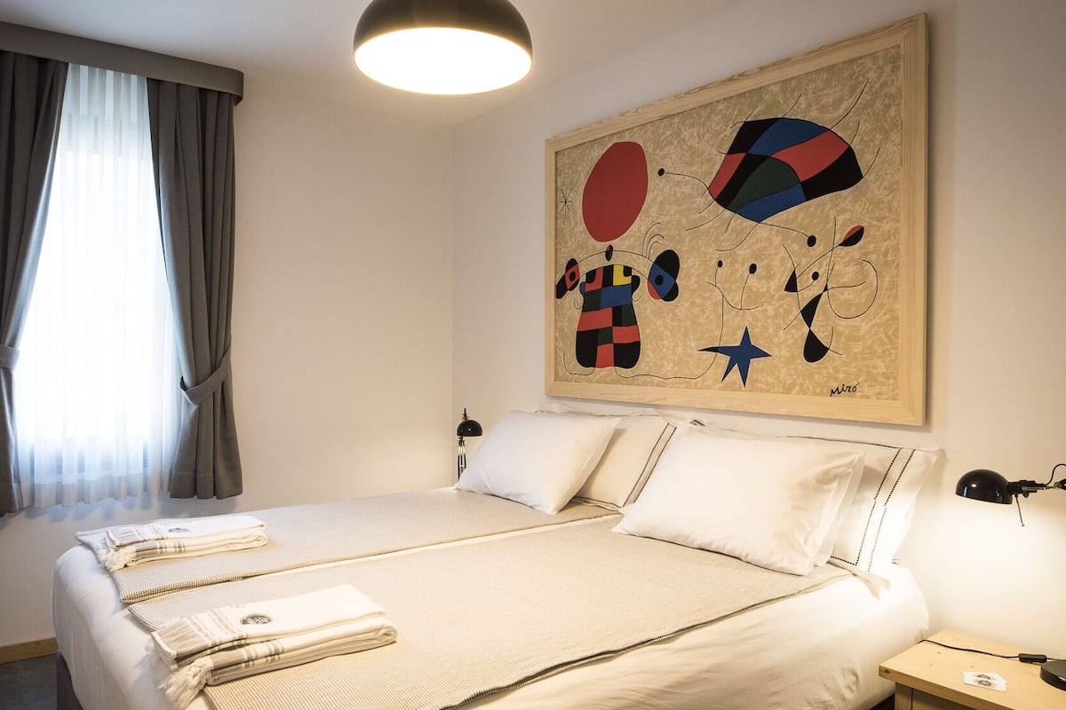 A hotel room with a large bed, a bedside table, a lamp, and a painting on the wall.