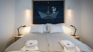 A neatly made bed with a large painting of a sailing ship and a crown above it, two bedside lamps, and a bedside table with a lamp. - Otel Fiori - Urla (Urla)