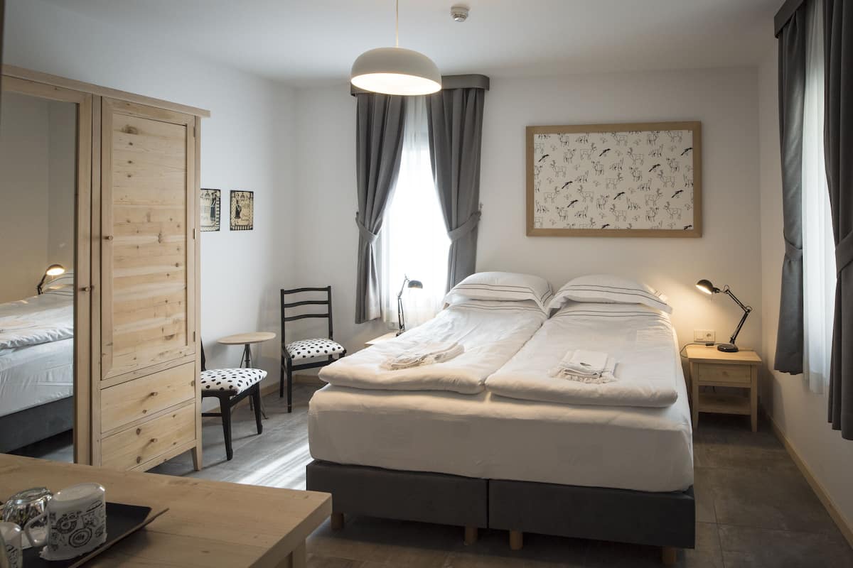 A neatly arranged bedroom with a bed, a wooden wardrobe, a chair, a small table, and a desk.