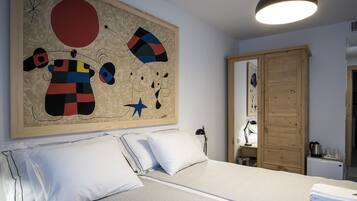Un dormitorio con cama, almohadas blancas, un cuadro abstracto grande, un armario de madera y un escritorio con lámpara.