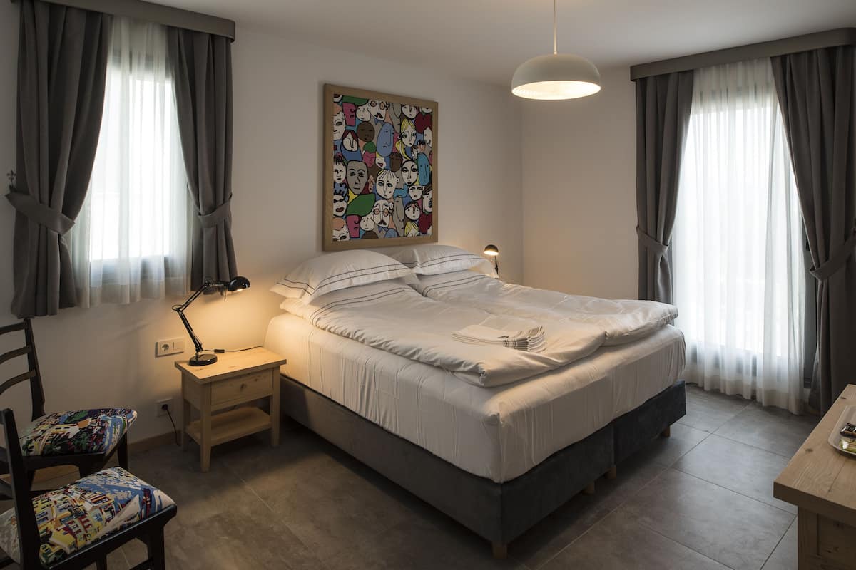A bedroom with a bed, bedside table, lamp, chair, and a colorful artwork on the wall.