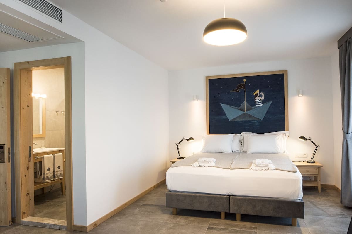 A modern bedroom with a large bed, bedside tables, a nightstand, a ceiling light, and a painting on the wall.
