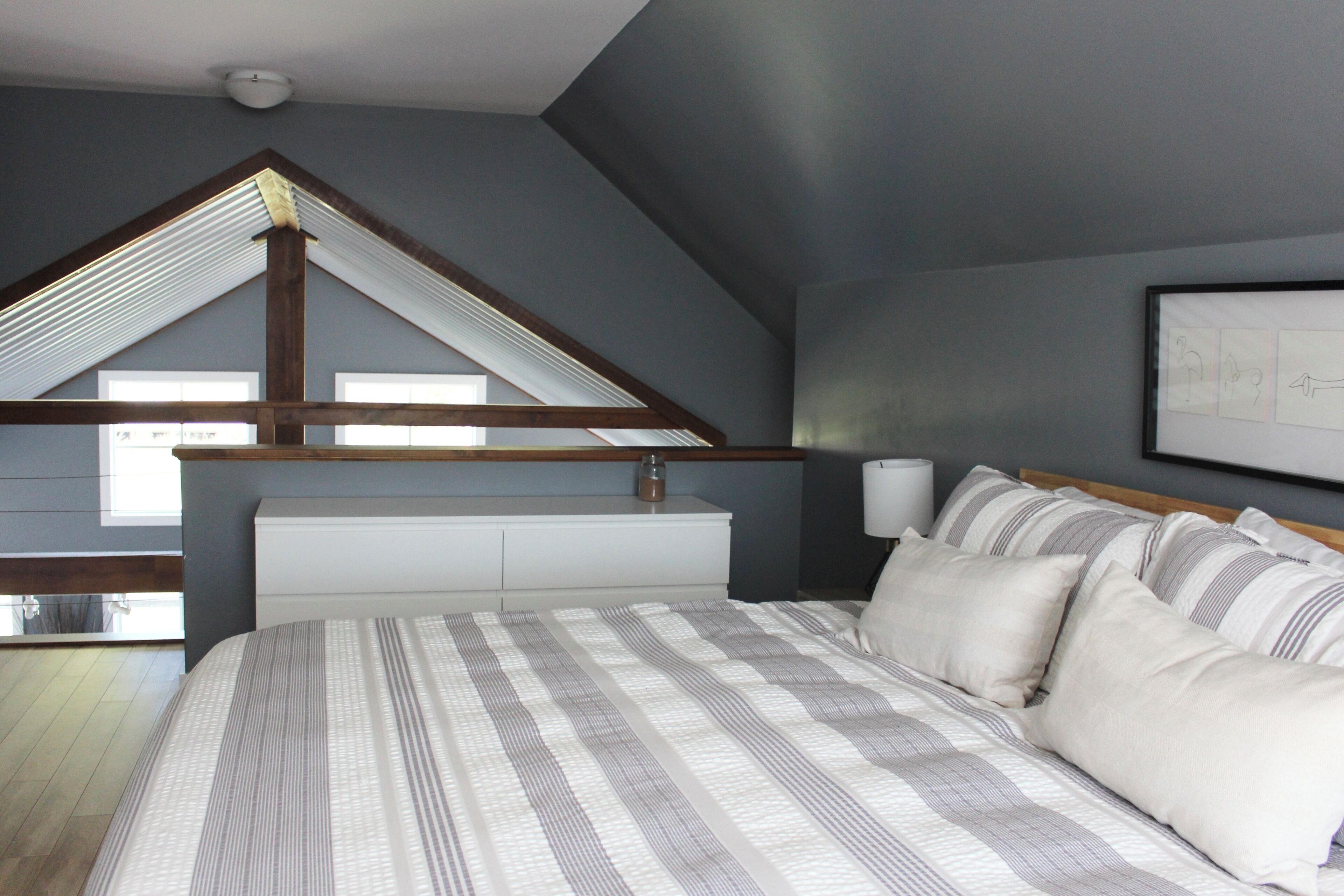 A bedroom with a sloped ceiling, a bed with striped bedding, a white headboard, and a framed picture on the wall.