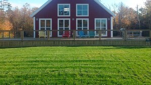 A two-story house with a red exterior and white trim, a fenced deck with chairs, and a well-maintained lawn.