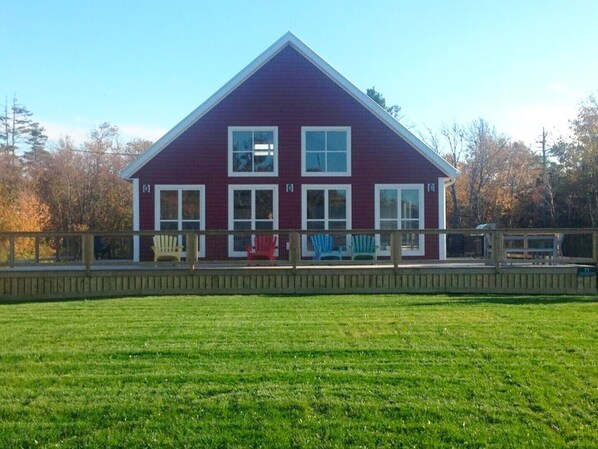 A two-story house with a red exterior and white trim, a fenced deck with chairs, and a well-maintained lawn.