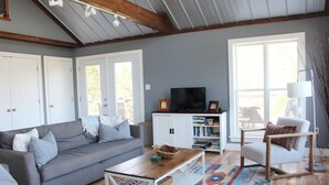 A living room with a grey sofa, a wooden coffee table, a white armchair, and a TV on a white cabinet.