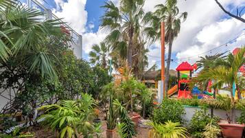 Un jardin tropical agrémenté de diverses plantes en pot et d’un espace de jeux pour enfants avec des toboggans colorés.