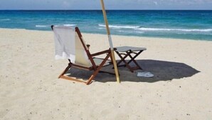 A beach with a white umbrella, a wooden chair, and a small table. - Ocean Gallery 26, Private Beach Access (St. Augustine)
