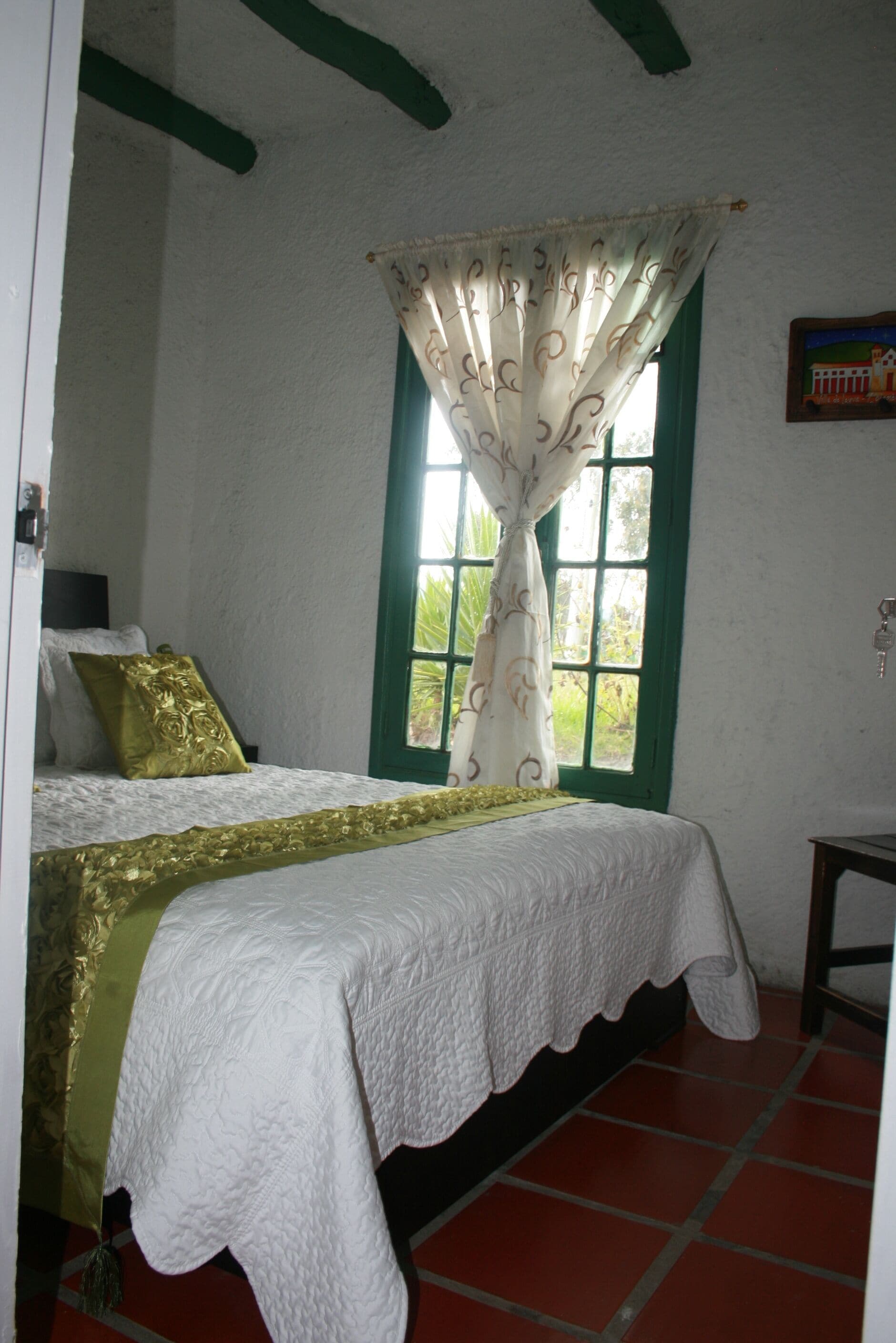 A bedroom with a bed, a window with curtains, a green wall, and a small table.