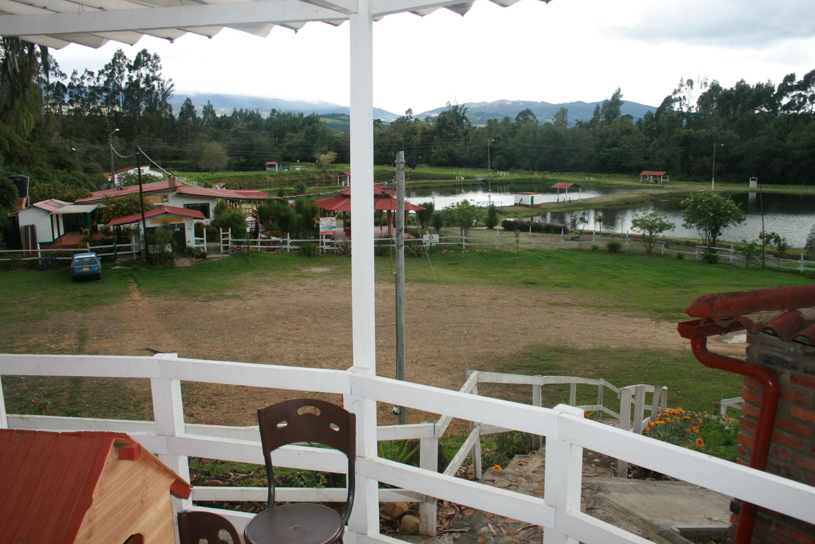 A covered outdoor area with a white fence, a chair, and a view of a lake and buildings in the background.