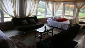 A cozy room with a sofa, a bed, a coffee table, and a chair. There are large windows with curtains. - Naturaleza Muisca Sas (Guasca)