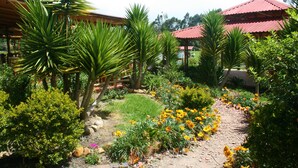 A garden with a paved path, various plants, and a building with a red roof. - Naturaleza Muisca Sas (Guasca)