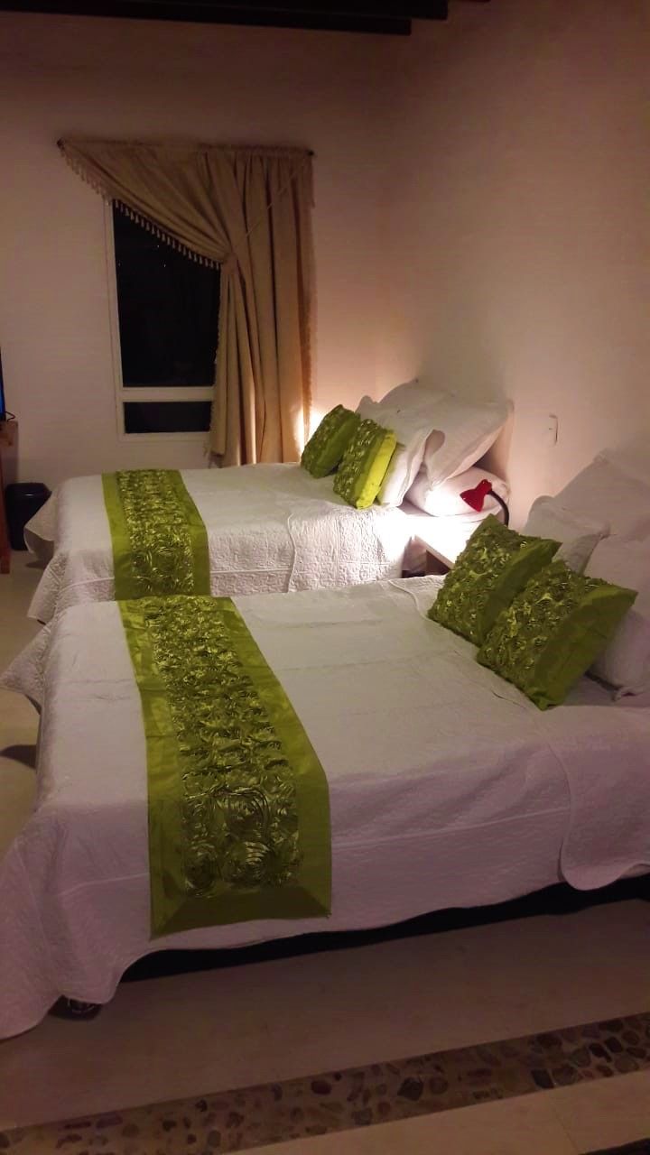 A double bed with green decorative pillows and a white bedspread in a room with a window and curtains.