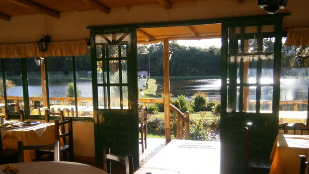 A restaurant with outdoor seating overlooking a lake, featuring wooden tables and chairs, and a view of the water and greenery. - Naturaleza Muisca Sas (Guasca)
