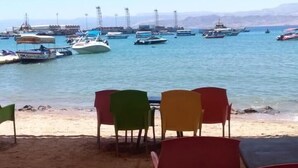 Uma área de estar à beira-mar, com mesas e cadeiras sob um toldo, com vista para uma marina com barcos.