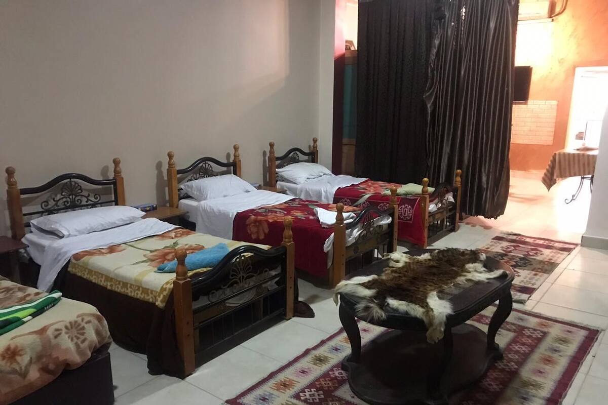 Habitación de hotel con cuatro camas individuales, un pequeño sofá y una alfombra estampada.