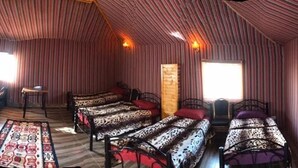 Quarto com várias camas, cada uma com roupa de cama estampada, paredes de madeira e duas janelas.