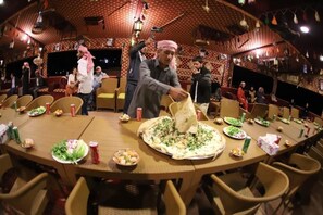 A restaurant with a large round table set for a meal, surrounded by wicker chairs.