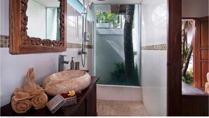Ein Badezimmer mit einem großen Spiegel, einer Holzausstattung, einem Steinkonstruktion-Waschbecken und einer Duschkabine mit Glastür.