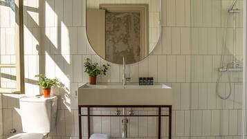 A bathroom with a toilet, sink, mirror, shower, and potted plant.