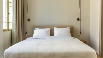 En pænt redt seng med hvide sengetæger i et rum med enkelt, rent design.
