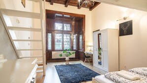 A bedroom with a large window, a bed, a desk, and a wardrobe.