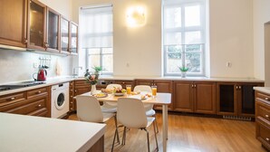 A modern kitchen with wooden cabinets, a built-in washing machine, a dining area with a table and chairs, and large windows providing natural light.
