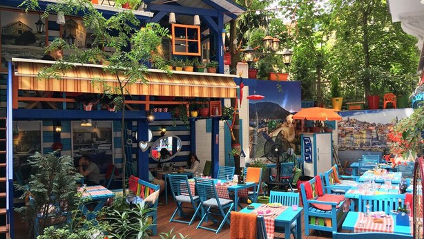 An outdoor café with blue furniture, potted plants, and a mural.