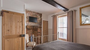 Ein Schlafzimmer mit Backsteinwand, Holztür, einem Bett, einem Sessel, einem Fernseher und einem Fenster mit Vorhängen.