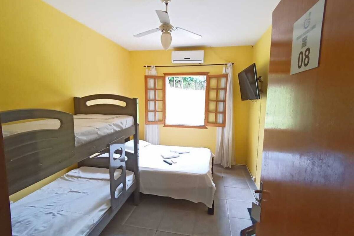 Una habitación con literas, ventilador de techo, aire acondicionado, televisor y una ventana con cortinas.