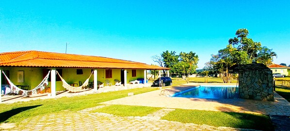Una casa con techo rojo, piscina y una construcción de piedra.