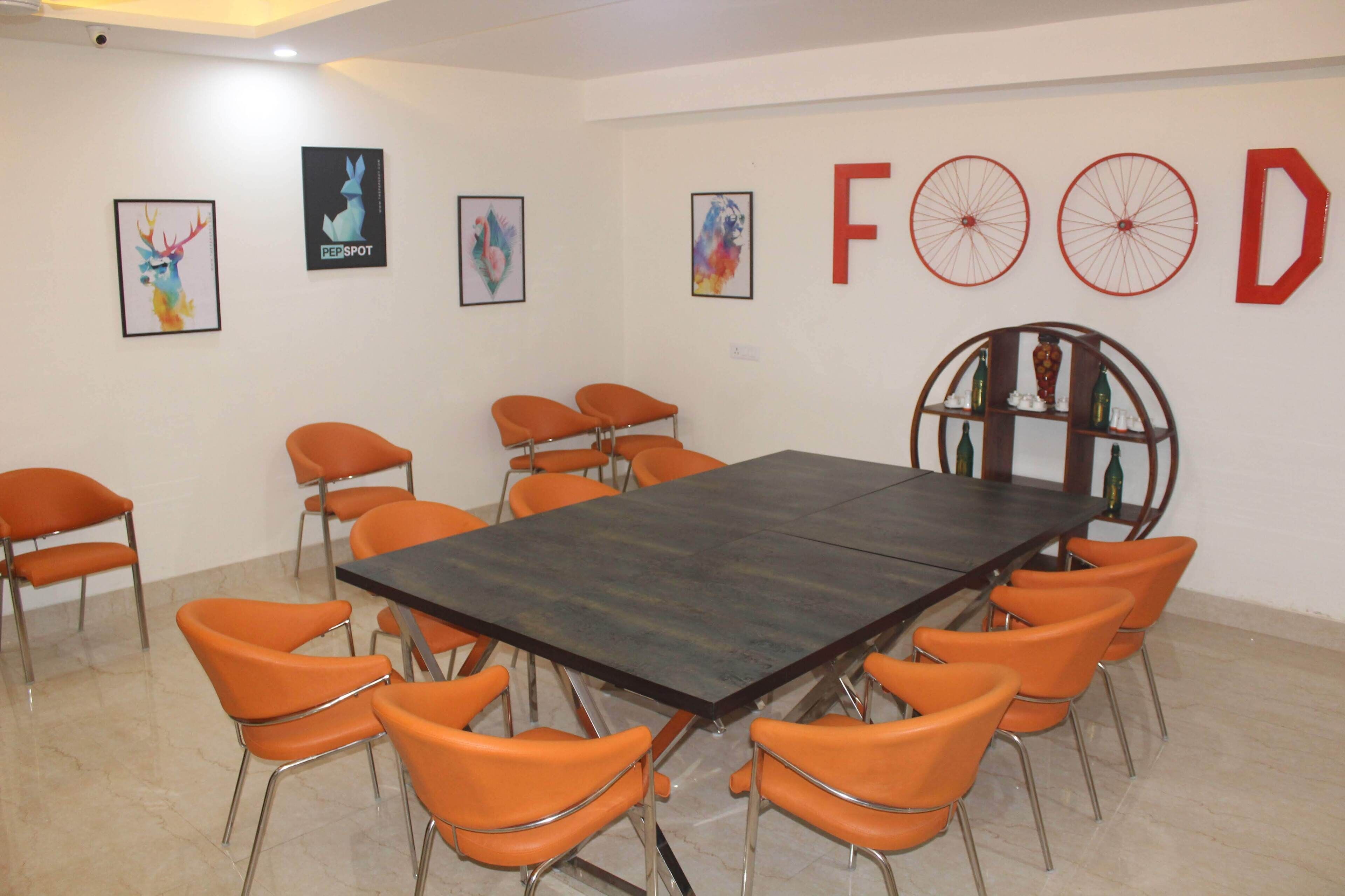 A conference room with a long table and orange chairs, framed artwork on the walls, and a large red letter 'D' decoration.
