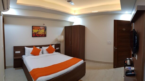 A modern hotel room with a large bed, wooden wardrobe, and a television. - PLLAZIO Residency (Gurugram)